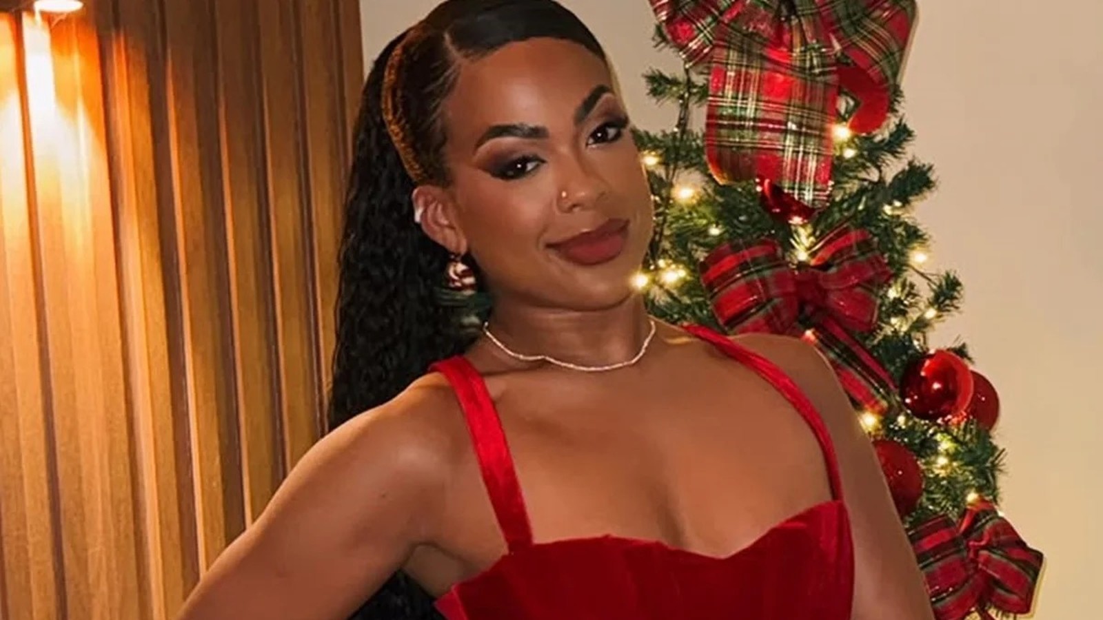 A cantora Marvvila sorri para a câmera com vestido vermelho e fundo de Natal