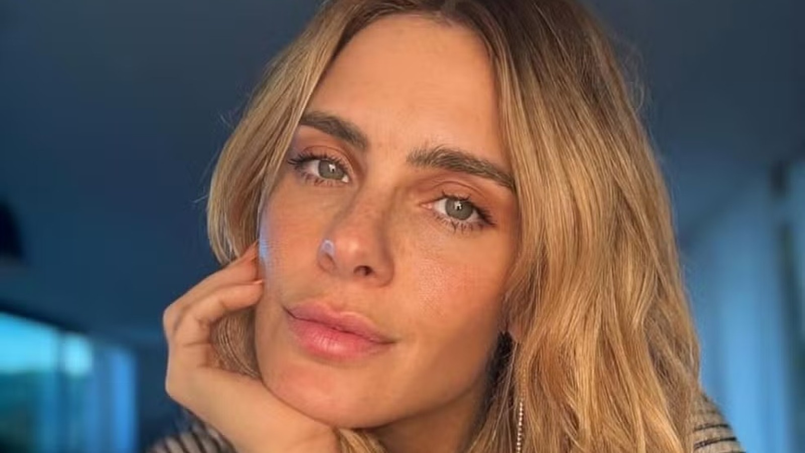 Close-up de Carolina Dieckmann, cabelo loiro, olhos claros, com a mão no rosto