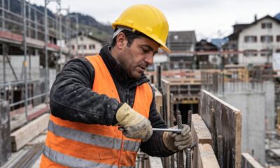 Homem trabalhador da construção civil, com capacete e colete, manipulando ferragens em canteiro de obras