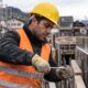 Homem trabalhador da construção civil, com capacete e colete, manipulando ferragens em canteiro de obras