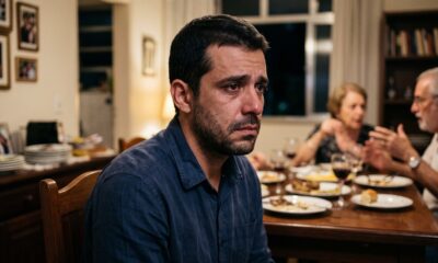 Homem com olhos marejados em jantar familiar, com pessoas desfocadas ao fundo