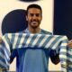 Homem sorrindo segura cachecol listrado azul e branco da Lazio, uniforme azul claro