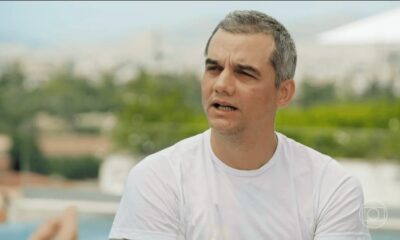Homem de meia-idade com cabelos grisalhos e camiseta branca, boca semiaberta, em ambiente externo