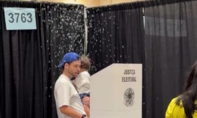 Homem com boné azul segura criança em urna eleitoral com bolhas. Texto "JUSTIÇA ELEITORAL" e "3763".