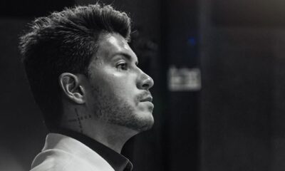 Arthur Aguiar em preto e branco, de perfil, cabelo escuro, barba e tatuagem no pescoço