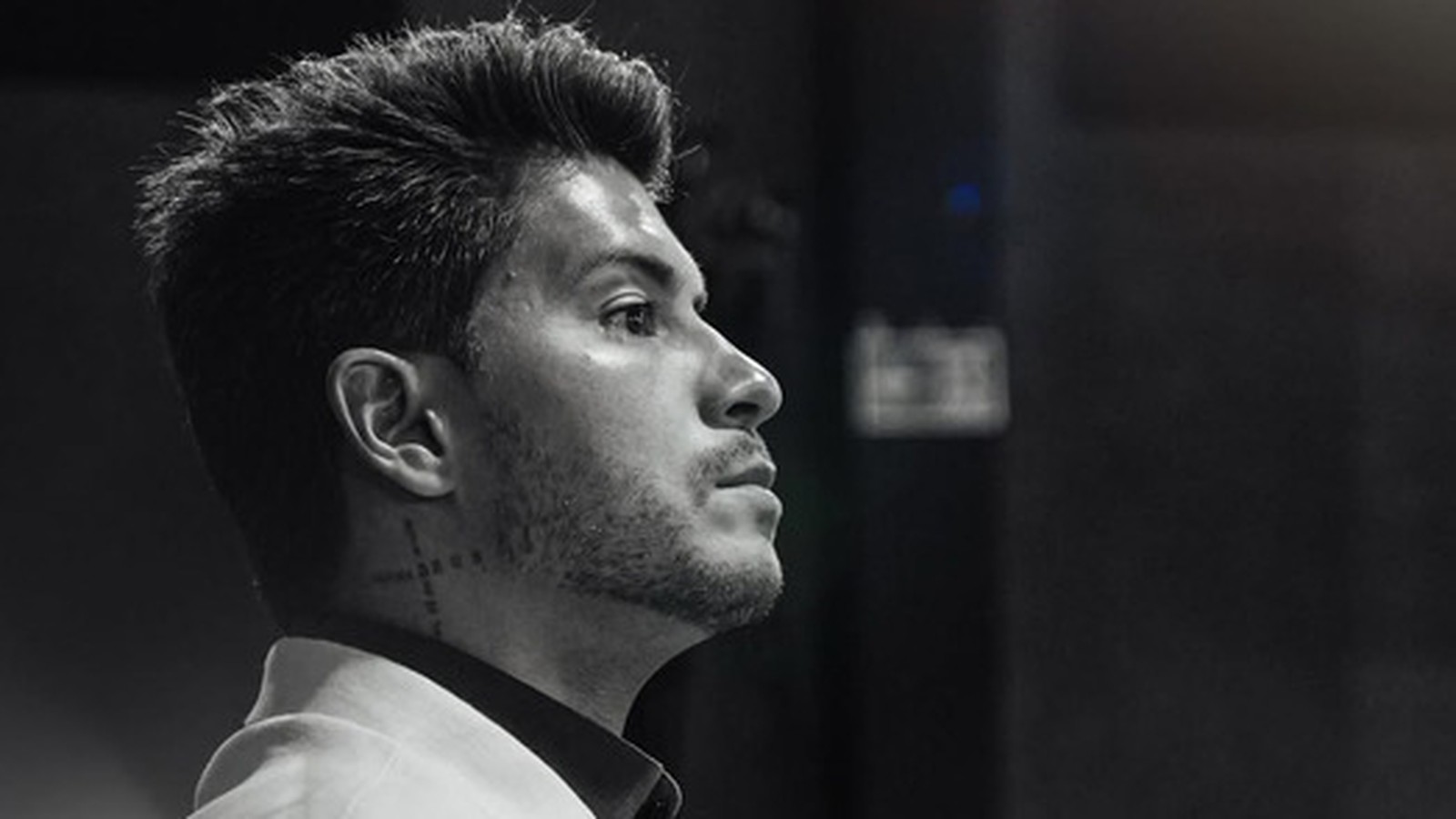 Arthur Aguiar em preto e branco, de perfil, cabelo escuro, barba e tatuagem no pescoço