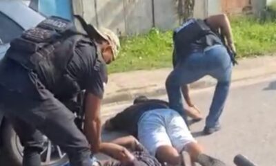 Dois agentes detêm dois homens deitados no chão na rua, ao lado de um carro