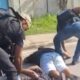 Dois agentes detêm dois homens deitados no chão na rua, ao lado de um carro