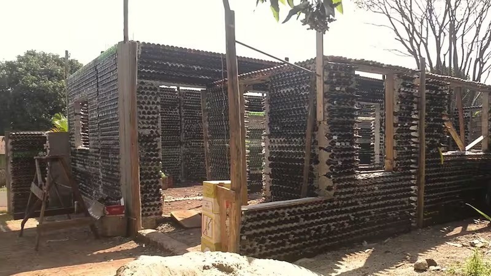 Casa em construção com paredes feitas de garrafas de vidro recicladas e estrutura de madeira aparente