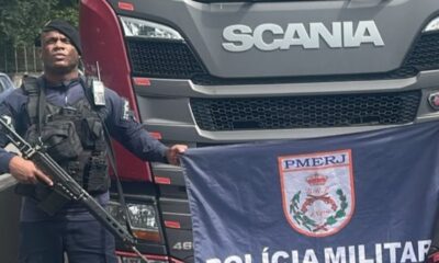 Policial com rifle e bandeira PMERJ à frente de caminhão Scania com logotipo e "46"