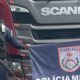 Policial com rifle e bandeira PMERJ à frente de caminhão Scania com logotipo e "46"