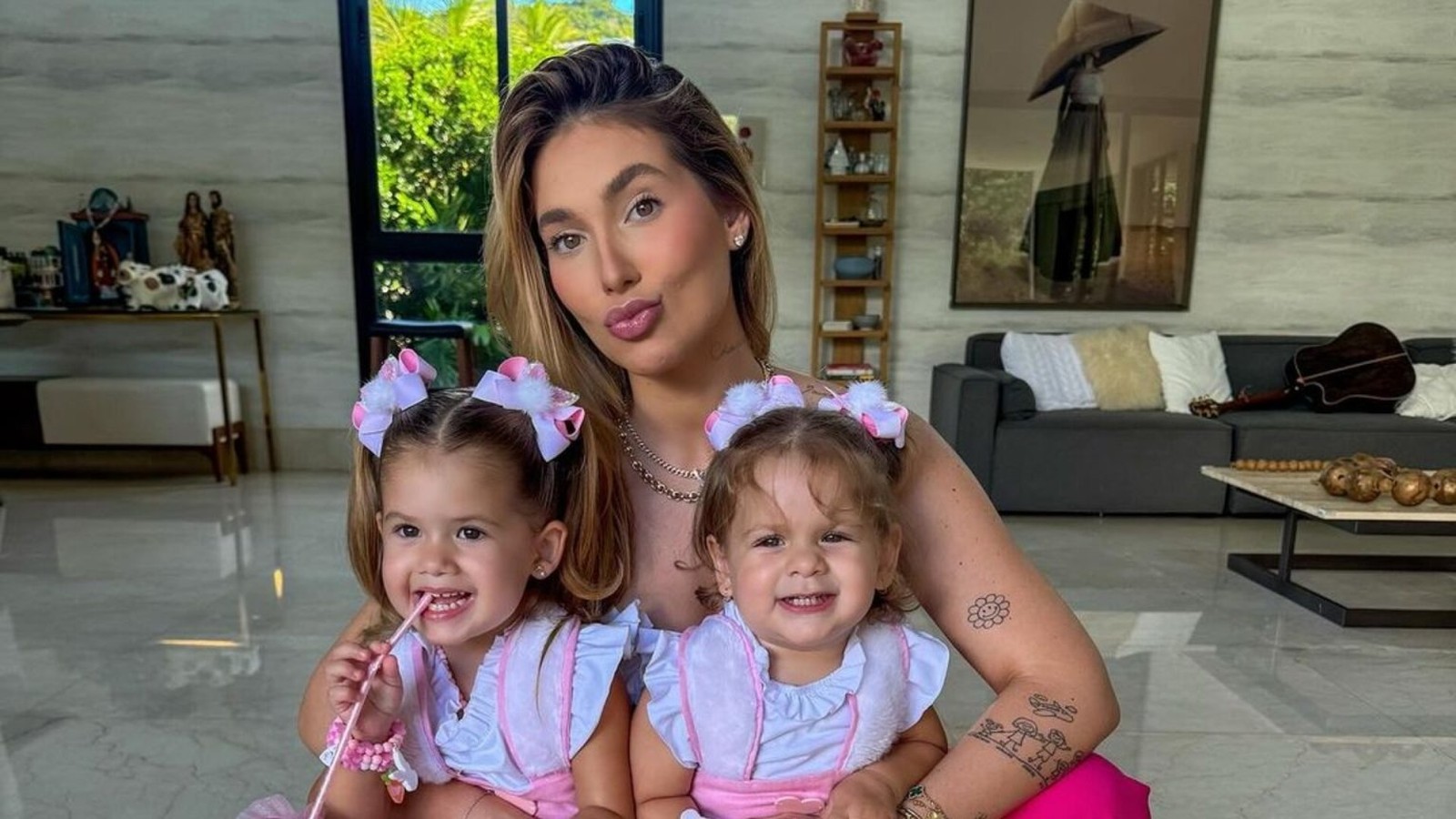 Mulher sorridente e duas meninas pequenas, vestindo roupas rosa idênticas e laços de cabelo combinando