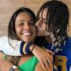 Rapper Oruam beija o rosto sorridente da mãe, Márcia Gama, com fundo de madeira