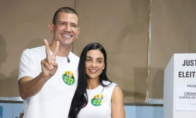 Douglas Ruas e Mariana Barbosa sorrindo, ele faz "V", com caixa "JUSTIC ELEITOF" no fundo.
