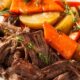 Prato com carne desfiada, batatas e cenouras assadas, guarnecido com alecrim e tomilho