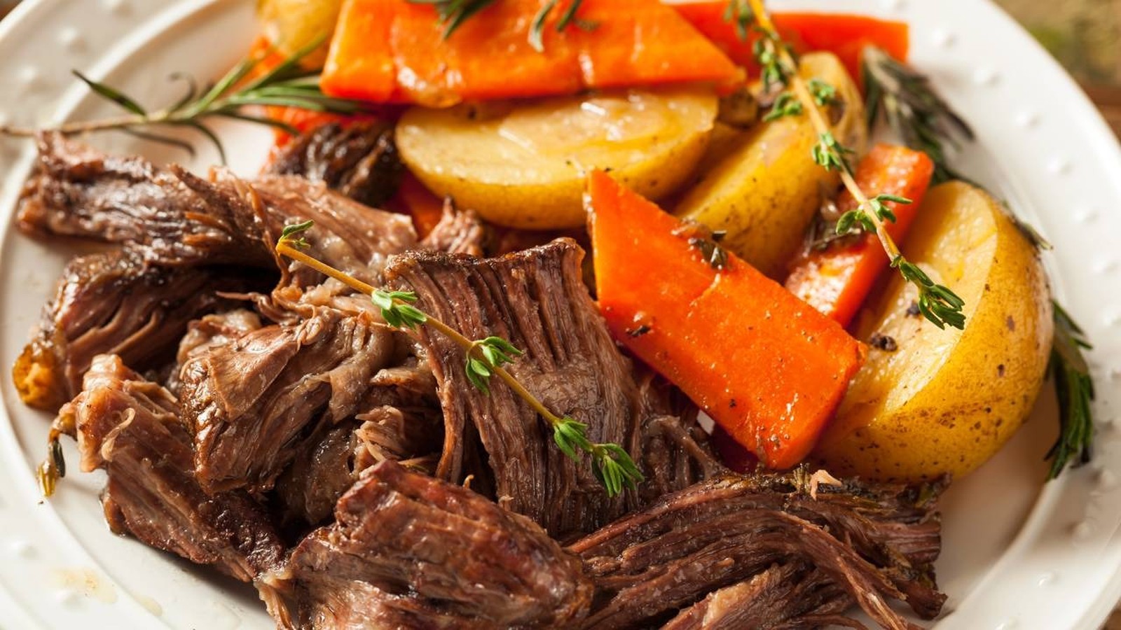 Prato com carne desfiada, batatas e cenouras assadas, guarnecido com alecrim e tomilho