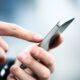 Mãos segurando um smartphone e um dedo indicador tocando a tela