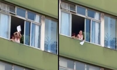 Mulher em janela de prédio verde tem cartaz branco tirado da mão, boca aberta