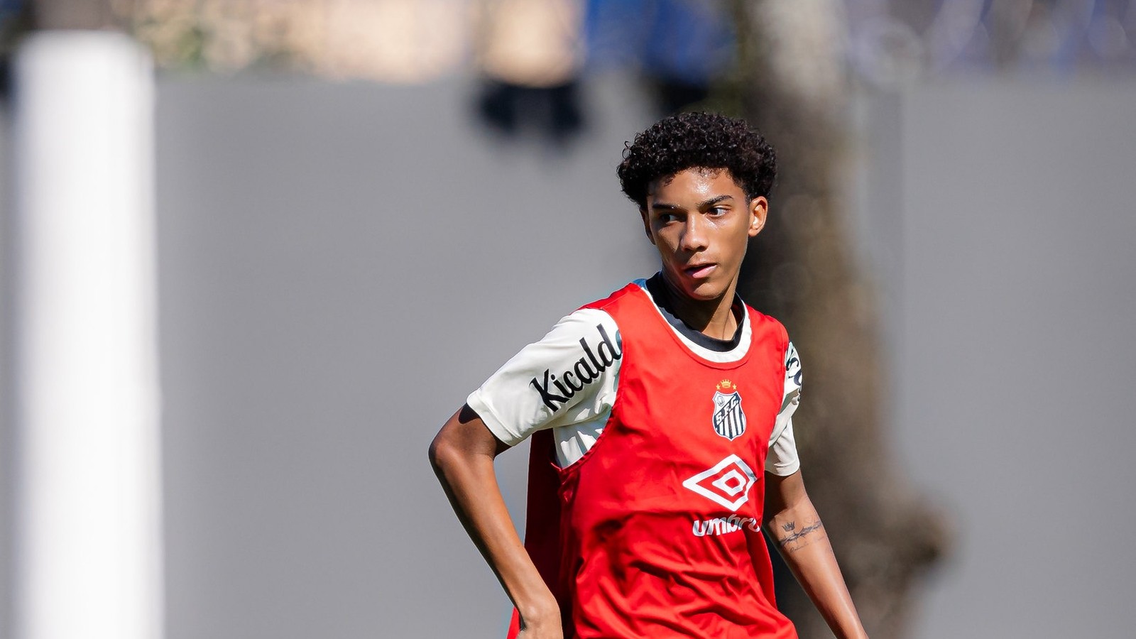 Jovem jogador com camisa "Kicald" e colete Santos FC, olhando para a esquerda