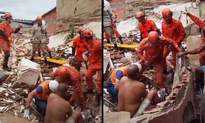 Bombeiros resgatam pessoas dos escombros de um prédio desabado, cercados por entulho e poeira