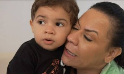 Mulher adulta com olhos fechados abraça menino pequeno com lágrima no rosto e cabelo cacheado