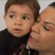 Mulher adulta com olhos fechados abraça menino pequeno com lágrima no rosto e cabelo cacheado