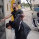 Suspeito algemado é conduzido por agente da Polícia Civil perto de carro
