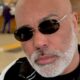 Close-up de homem careca com barba grisalha e óculos escuros Ray-Ban com '72'