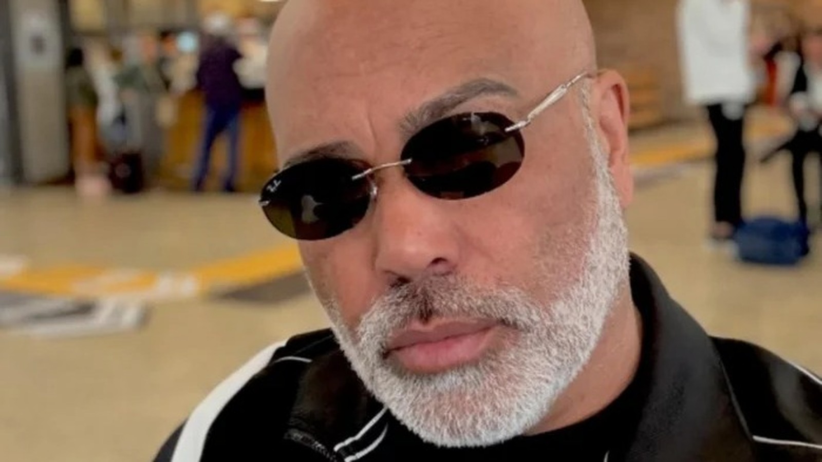 Close-up de homem careca com barba grisalha e óculos escuros Ray-Ban com '72'