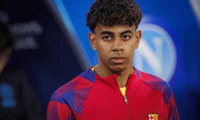 Jovem homem de cabelo encaracolado vestindo camisa vermelha e azul do Barcelona, olhando à frente