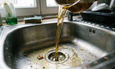 Líquido dourado escorrendo de uma panela para o ralo de uma pia de cozinha de aço inoxidável