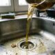 Líquido dourado escorrendo de uma panela para o ralo de uma pia de cozinha de aço inoxidável