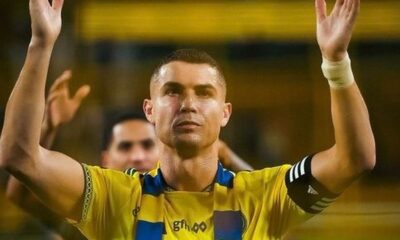 Cristiano Ronaldo com cabelo raspado, camisa amarela e azul, braços levantados com as mãos abertas