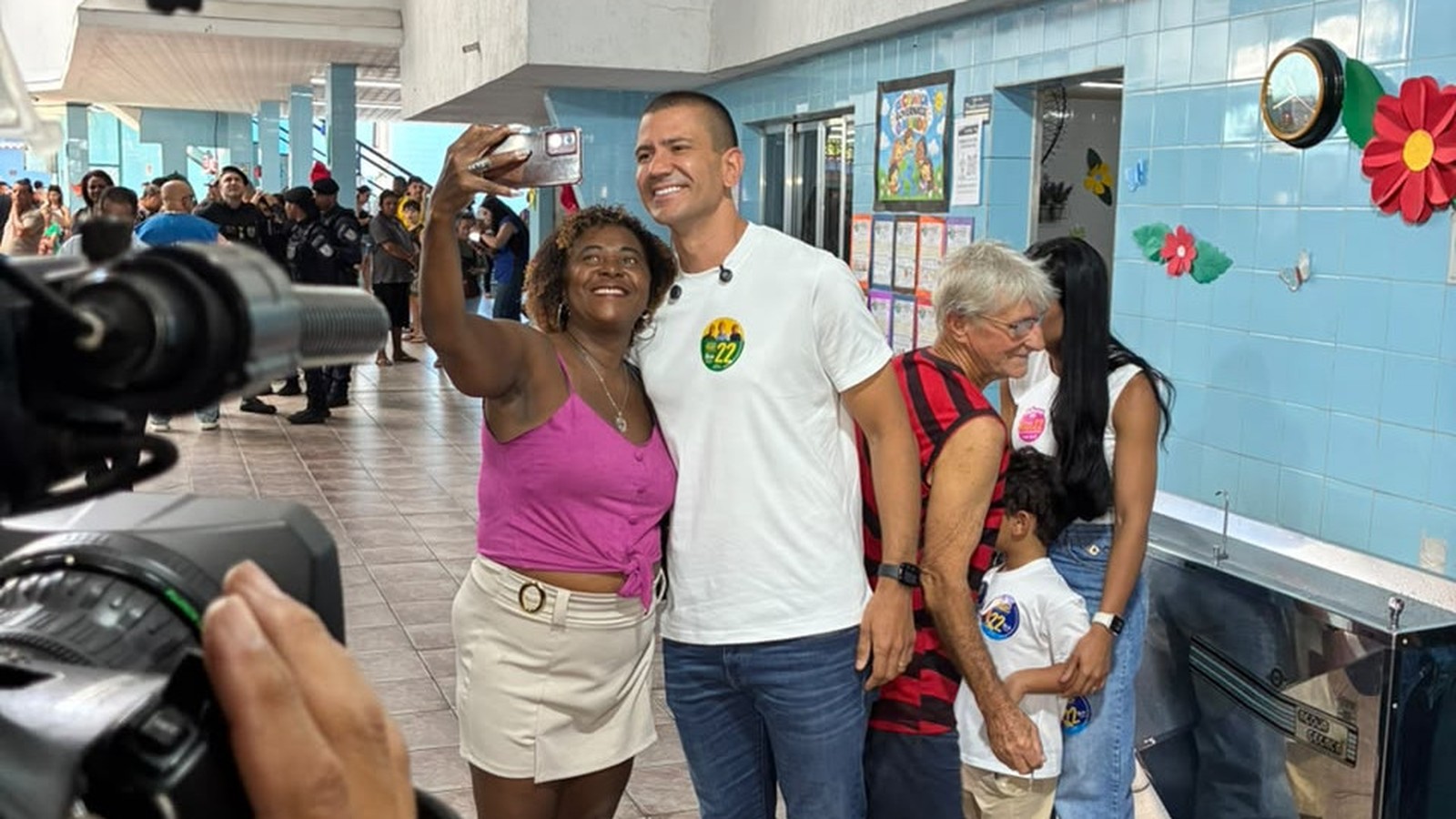 Douglas Ruas sorri em selfie com eleitora, usando camiseta com adesivo '22'