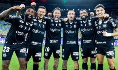Seis jogadores do Santos sorriem e celebram em campo, vestindo uniformes pretos