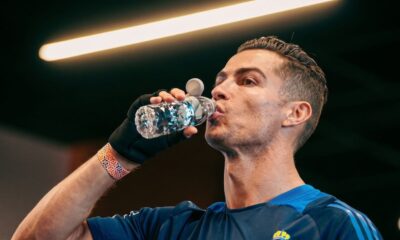 Cristiano Ronaldo bebe água de uma garrafa transparente com design facetado, usando camisa azul