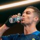 Cristiano Ronaldo bebe água de uma garrafa transparente com design facetado, usando camisa azul