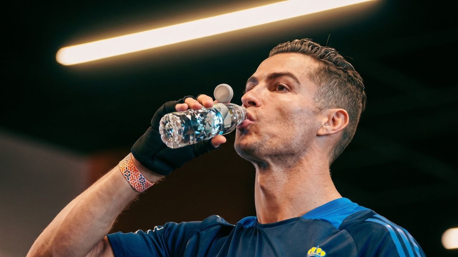 Cristiano Ronaldo bebe água de uma garrafa transparente com design facetado, usando camisa azul