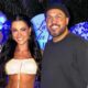 Rayane Figliuzzi e Belo, sorrindo, em festa com balões azuis e brancos, fundo com letreiro