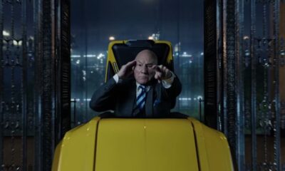 Patrick Stewart, careca, em cadeira amarela, terno, mão na têmpora e apontando