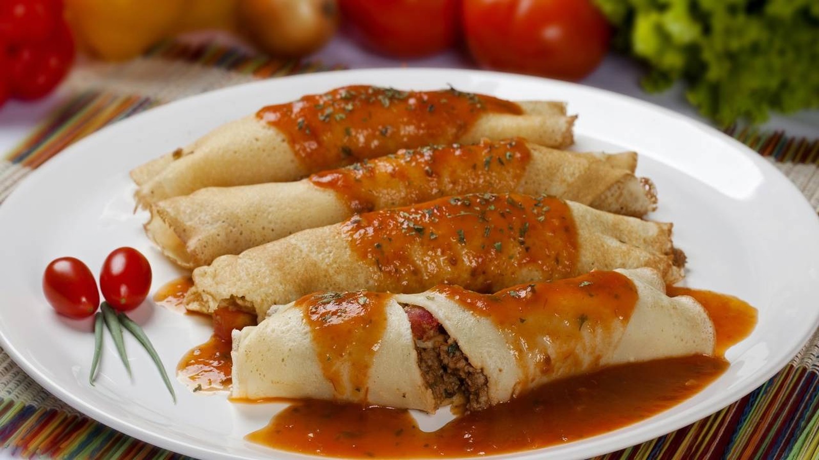 Quatro panquecas de carne moída com molho de tomate, guarnecidas com tomates cereja em prato branco