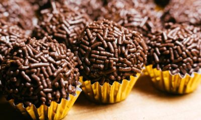 Vários brigadeiros de chocolate enrolados, com granulado e em forminhas douradas, em destaque