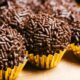 Vários brigadeiros de chocolate enrolados, com granulado e em forminhas douradas, em destaque