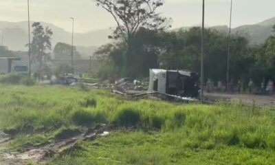 Caminhão branco tombado em acostamento de rodovia, com detritos e grama ao redor