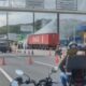 Caminhão Coca-Cola vermelho com água sendo jorrada, fumaça, cones, viatura PRF e prédio policial