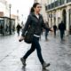 Mulher de jaqueta e jeans caminha em rua movimentada da cidade com garrafa d'água