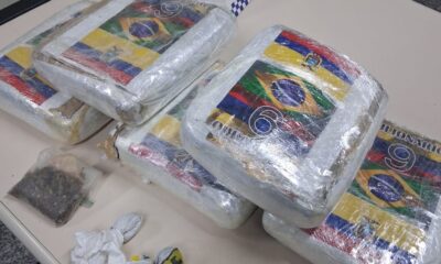 Blocos de maconha prensada com adesivos de bandeiras e 'MILIONARIO 9', e um saco pequeno de erva