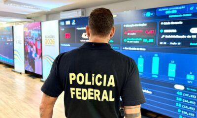 Policial Federal de costas observa painel de controle com dados e gráficos sobre as eleições 2026