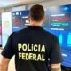Policial Federal de costas observa painel de controle com dados e gráficos sobre as eleições 2026