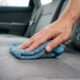 Mão de uma pessoa segurando pano de microfibra azul limpando assento cinza de carro